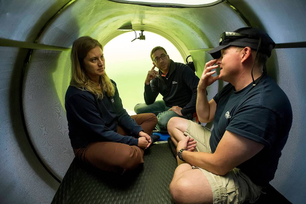David Lochridge (right) describes diving at great depths to Bonnie Carl and Josh Dean as they sit in the OceanGate sub Cyclops1 submerged in the waters of the Port of Everett Marina on May 18. (Andy Bronson / The Herald)