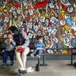 Ransom Butaud (left), his mother, Eleya Butaud, and brother, Sam Butaud, enjoy the sights and sounds of the concourse in front of a 24-foot long porcelain enamel mural called &ldquo;The Crowd.&rdquo; (Kevin Clark / The Herald)