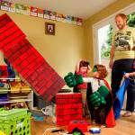 Little Seirsha knocks down a stack of boxes with one blow of her mighty Hulk gloves. Her mom painted those boxes to look like a chimney, just one of many such homemade playthings and costumes in the basement. (Dan Bates / The Herald)