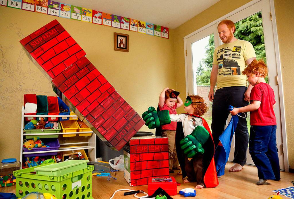 Little Seirsha knocks down a stack of boxes with one blow of her mighty Hulk gloves. Her mom painted those boxes to look like a chimney, just one of many such homemade playthings and costumes in the basement. (Dan Bates / The Herald)