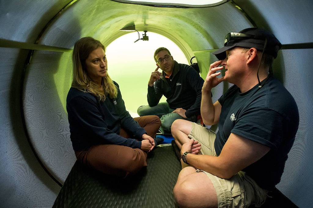 David Lochridge (right) describes diving at great depths to Bonnie Carl (left) and Josh Dean in the OceanGate sub Cyclops I, submerged in the waters of the Port of Everett Marina. (Andy Bronson / The Herald)