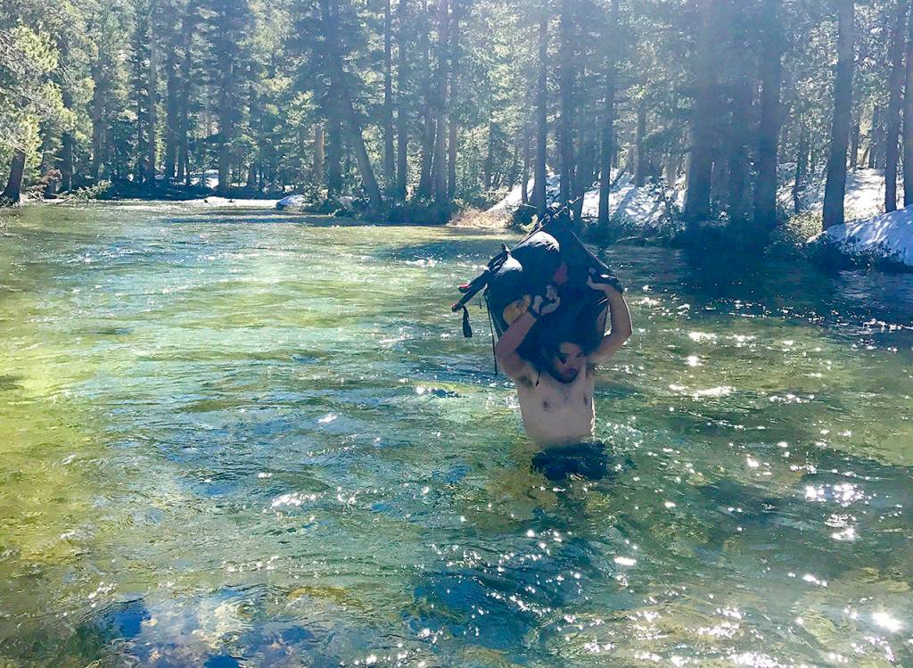 In this June 15 photo, Jake Gustafson crosses wading chest-deep in still waters with his backpack over his head at Evolution Creek along the Pacific Crest Trail near Kings Canyon National Park, California. (Wesley Tils via AP)