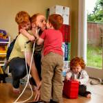In their basement playroom Thursday morning, Alex Clawson, 32, grants a kiss to son Atley, 3, while son Willem, 4, climbs up his back and 20-month-old daughter Seirsha tries to open a plastic container. (Dan Bates / The Herald)