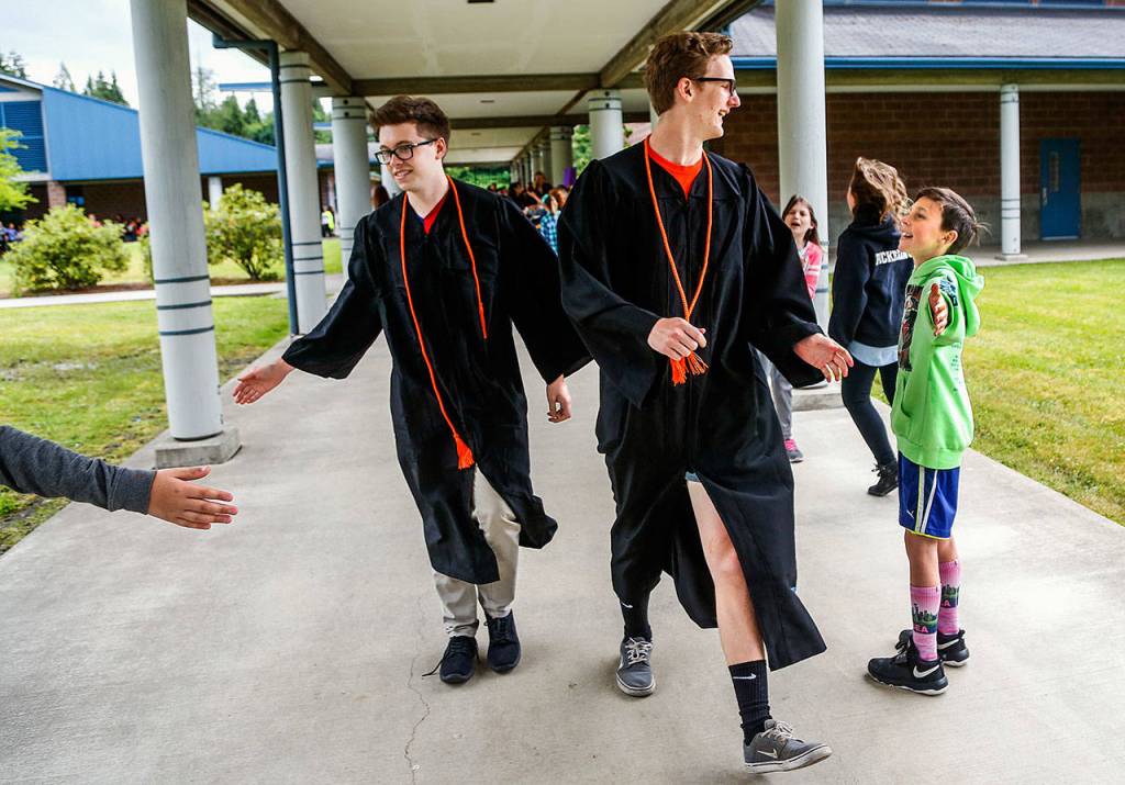 Monroe High School graduating senior Ethan Medlin (right) gets a big greeting from fourth-grader Jacob Shafer as he and classmate Dawson Eifert (left) and others walk the breezeways at Chain Lake Elementary School in their graduation gowns. (Dan Bates / The Herald)