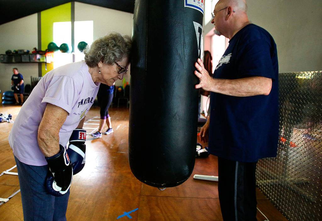 Volunteer assistant Rod Kleitz waits a moment for Donna Thorp, 83, of Lynnwood, to get a second wind during a workout on the heavy bag. (Dan Bates / The Herald)