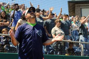Wearing an AquaSox jersey and hat, New Life Church Lead Pastor Jim Romack prays along with members of the church during a song played by the church&rsquo;s band at the One Day event held at Everett Memorial Stadium Ballfield on Sunday. (Doug Ramsay / for The Herald)
