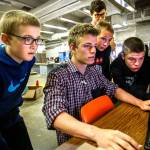 In the Granite Falls Middle School&rsquo;s shop building, manufacturing teacher Kirk Parker (back left) watches seventh and eighth-grade students, Jamieson Haverfield (left) Malachi Caldera, Dylan Klepper, Parker Lembke and Derek Caldart (standing) who are fully engrossed as Caldera, using a computer, sets up the parameters of a laser printer that will enable them to engrave their designs on wood. The building is going to be remodeled next year to better accommodate teaching manufacturing technologies like this. (Dan Bates / The Herald)