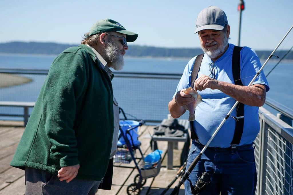 Kayak Point campground host Lamont Olson (left) checks out park-goer Mike Wilcox&rsquo;s flounder catch on the dock on June 22. (Ian Terry / The Herald)
