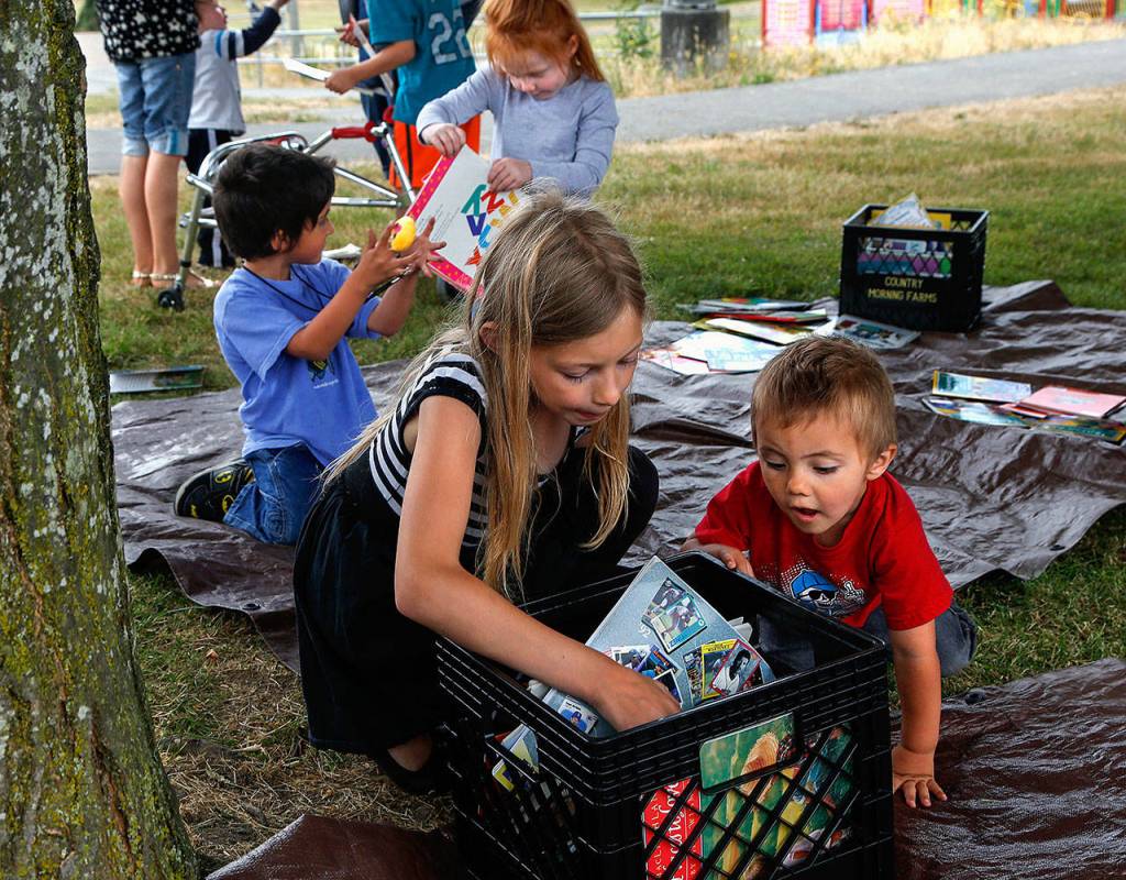 Alysah Burkett, 8, (left foreground) attracts the interest of her little brother, Ezra Burkett, 2, while going through bins full of books that she might like to read. (Dan Bates / The Herald)