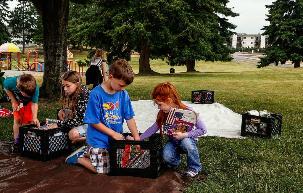 From left, Isaiah Burkett, 5, Leah Burkett, 10, Micah Burkett, 6 and Eliana Puterbaugh, 4, go through crates filled with books Thursday at Wiggums Hollow Park where Hawthorne Elementary School&rsquo;s Assistant Principal Valerie Yob and teacher-librarian Liz Trujillo have been holding a children&rsquo;s book opportunity each week. (Dan Bates / The Herald)