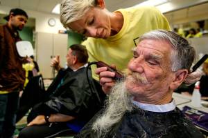 After giving him a haircut Thursday, Paroba College of Cosmetology and Barbering student Sommer McKenzie removes the full beard, along with some years, from the face of Rick Young, who has been staying at the Everett Gospel Mission the past month. In the background, fellow student Davonte Peterson holds a mirror for Matthew Clark, 50, who gives a thumbs up to the new haircut. (Dan Bates / The Herald)