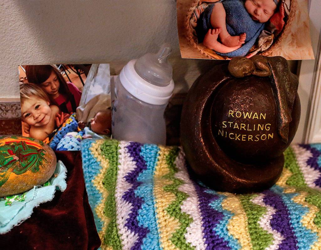 An urn holding baby Rowan&rsquo;s ashes sits at one end of the kitchen counter with other momentos, including a photo of the other children with newborn Rowan. The baby blanket in the photo is also on the counter. (Dan Bates / The Herald)