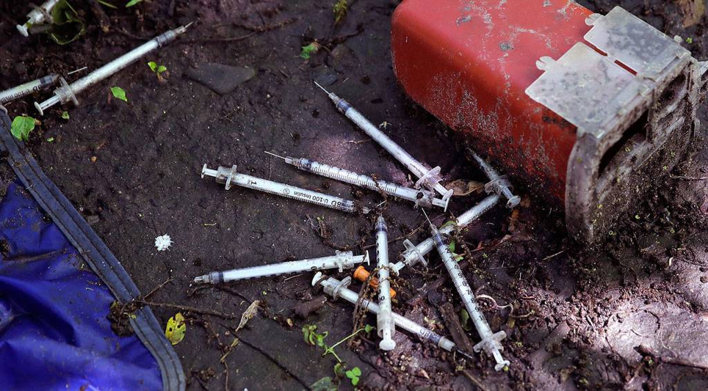 This Wednesday, June 7, 2017 photo shows discarded used hypodermic needles without protective sheaths at an encampment where opioid addicts shoot up along the Merrimack River in Lowell, Mass. Syringes left by drug users amid the heroin crisis are turning up everywhere. They hide in weeds along hiking trails and in playground grass, get washed into rivers and onto beaches, and lie scattered about in baseball dugouts and on sidewalks and streets. There are reports of children finding them and getting poked. (AP Photo/Charles Krupa)