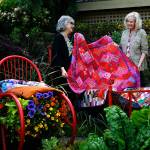 Quilters Kay Davidson (left) and Sydney Hoard test place some of their quilts on an iron bed frame in Janice Tallman&rsquo;s featured garden. The quilt they are lifting up is Hoard&rsquo;s and is titled &ldquo;Dahlias, and Then Some.&rdquo; (Dan Bates / The Herald)