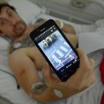Bill Hillmann, 35, lying in a hospital bed, shows a photo of himself that someone sent to him during a bull run a day before he was gored Saturday. (AP Photo/Alvaro Barrientos)