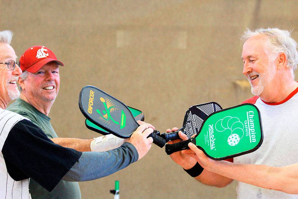 After a game, players Clare Kruse, Dave Meyer, and Barry Haworth (left to right) give the customary high-five slap of their pickle ball racquets. Getting together twice a week to play pickle ball is good for friendships and fitness, say about 30 participants of the Oak Harbor Senior Center activity. (Patricia Guthrie/Whidbey News-Times)