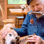 Peter Lawlor and his dog, Claude, are Saturday morning regulars at Cafe in the Woods near Langley. For customers, he plays and sings songs of the sea from his worldwide travels. The native New Zealander, 95, has lived in Clinton the past dozen years. &ldquo;I&rsquo;m proud of my age,&rdquo; he says. &ldquo;I think I&rsquo;ve had a good go.&rdquo; (Patricia Guthrie/Whidbey News-Times)