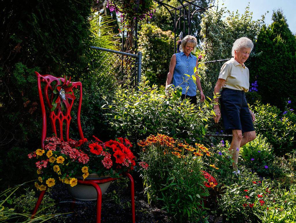 Janice Tallman follows next-door neighbor Marilyn Larson through a gate that connects their gardens and down a sloped trail. Larson&rsquo;s garden (showing this side of the gate) is also part of the tour. (Dan Bates / The Herald)