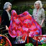 Quilters Kay Davidson (left) and Sydney Hoard test place some of their quilts on an iron bed frame in Janice Tallman&rsquo;s featured garden. The quilt they are lifting up is Hoard&rsquo;s and is titled &ldquo;Dahlias, and Then Some.&rdquo; (Dan Bates / The Herald)