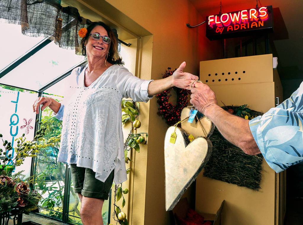 From a store window display, Paula Adrian takes down and hands the last of her birch framed hanging hearts to husband Bob Monday after they were purchased by longtime customer Jeannie Sears. (Dan Bates / The Herald)