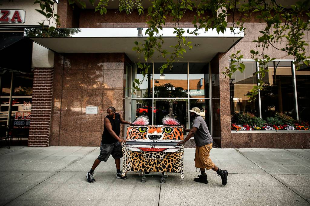 Piano movers Alton Johnson (left) and KJ Butler roll a piano down Colby Avenue in Everett for installation on Wednesday, Aug. 2. (Ian Terry / The Herald)