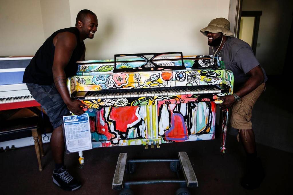 Alton Johnson (left) and KJ Butler, movers from The Piano & Organ Moving Company, hoist a piano up before delivering it to its final location in downtown Everett on Wednesday, Aug. 2. (Ian Terry / The Herald)
