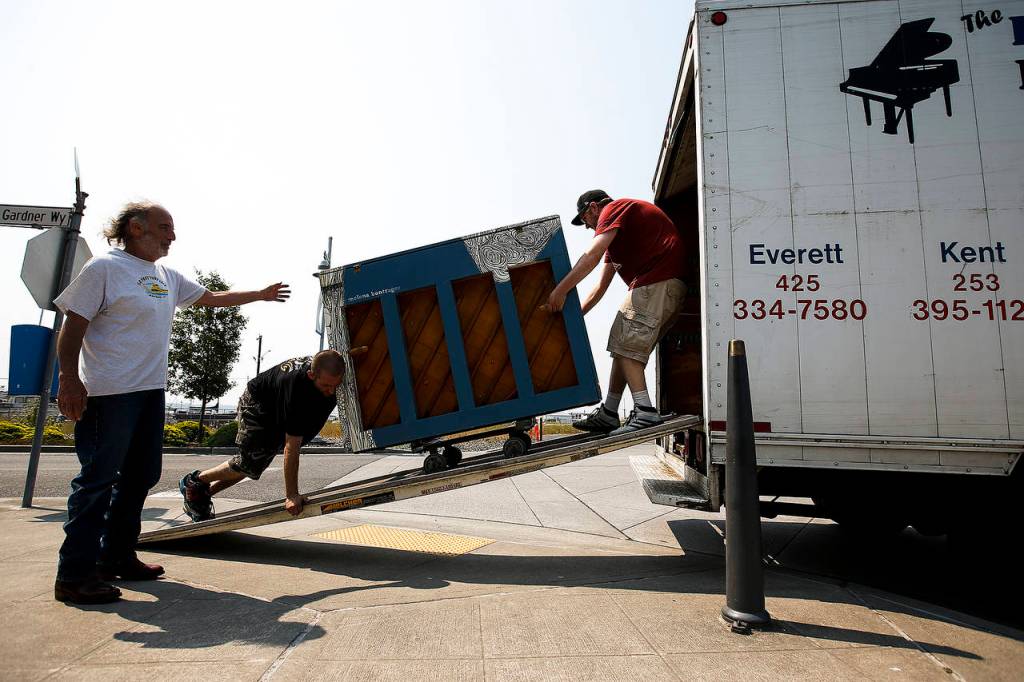 Mike Alkire (left) directs Dan Demascio (center left) and Robert Alkire as they roll out a piano to be placed in front of Scuttlebutt Brewery on the Everett waterfront on Wednesday, Aug. 2. (Ian Terry / The Herald)