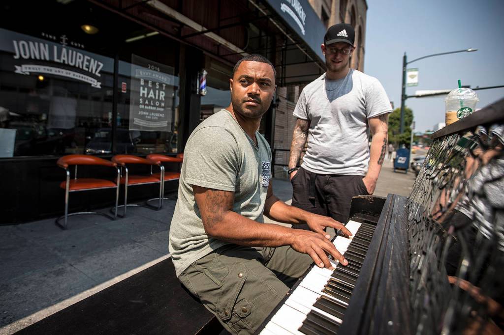 Erik Richerson (center), owner of Jonn Laurenz Fine Cuts, plays a tune as Aaron Davis listens on Wednesday, Aug. 2 in downtown Everett. (Ian Terry / The Herald)