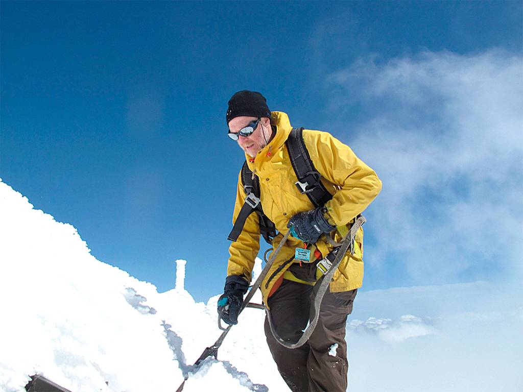 Dan Jaffe climbs on the roof of the summit building at Mount Bachelor to set up air inlet lines to collect samples for weather research. (Photo by James Dennison)