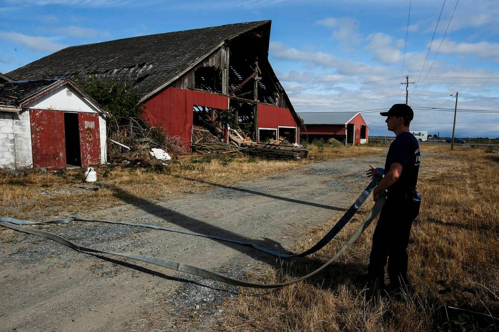 North County fireman John Estep prepares a hose for a practice burn of an old barn on the Ovenell property in Stanwood on Friday, Aug. 18. (Ian Terry / The Herald)