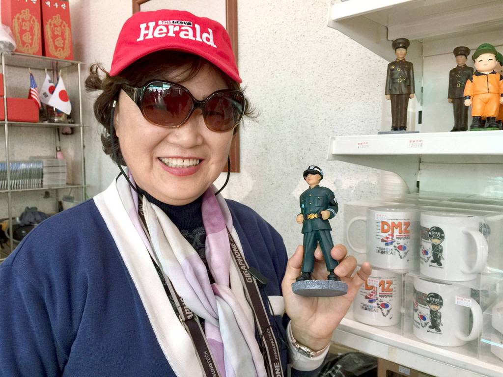The South Korean tour guide at the DMZ proudly wore a Herald hat and held a statue of a South Korean soldier at the souvenir shop. She would not hold a North Korean soldier, shown on the shelf above. (Andrea Brown / The Herald)