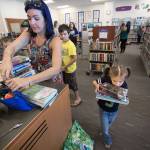 As her mother, Ande, looks for her library card, Magdalena Gaiten, 5, carries a heavy load of books to the checkout counter at Mariner Library on Monday in Everett. The family of four kids checked out 27 books from the library, which they visit weekly. (Andy Bronson / The Herald)