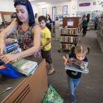 As her mother Ande looks for the library card, Magdalena Gaiten, 5, carries a heavy load of books to the checkout counter at Mariner Library on Monday, Aug. 21, 2017 in Everett, Wa. The family of four kids checked out 27 books from the library where they make a trip weekly for new books.(Andy Bronson / The Herald)