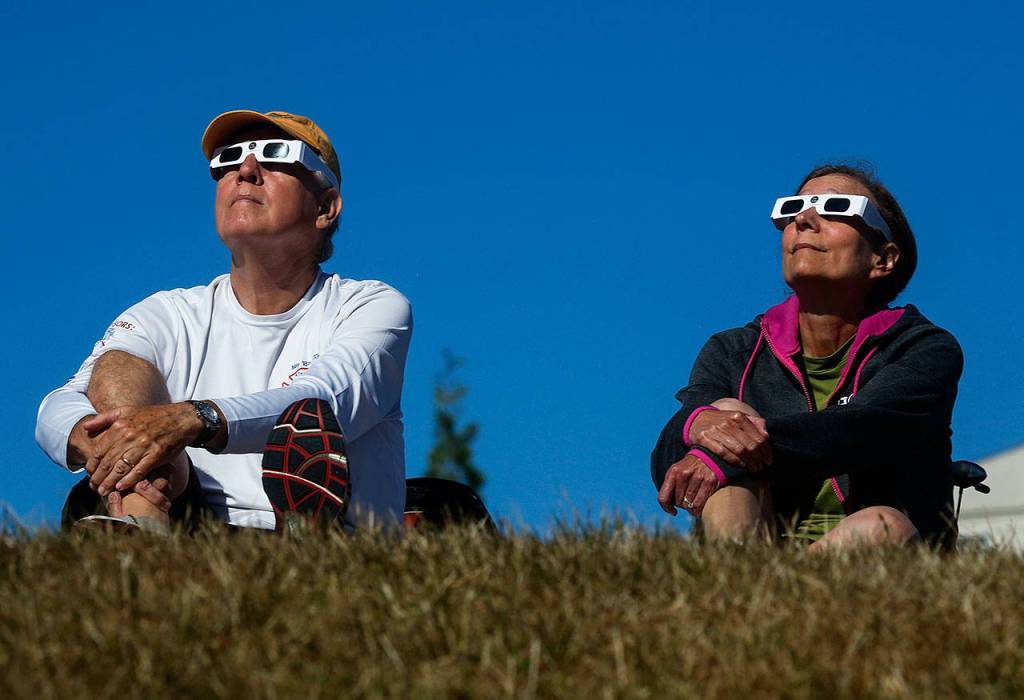 At 10:17 a.m., a few minutes before the greatest extent of the eclipse in Snohomish County on Monday, Tom and Jan Osterwald of Mukilteo watch the solar eclipse from a grassy berm next to the Future of Flight Aviation Center at Paine Field. (Dan Bates / The Herald)