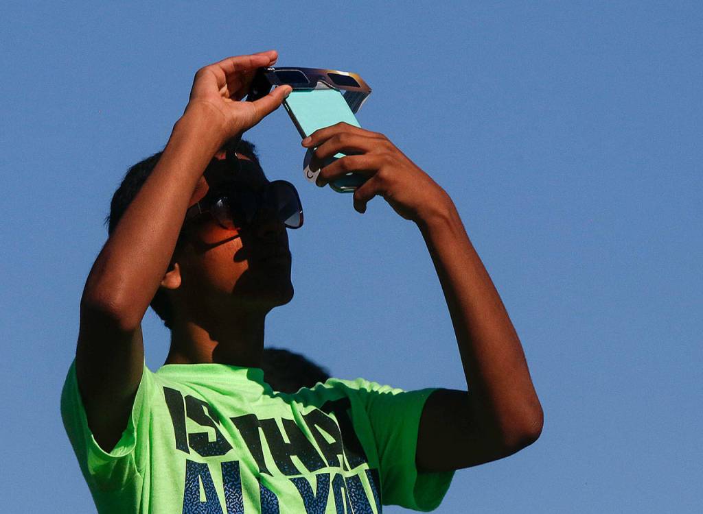 A young man takes a phone photo through the filter of his protective eyewear on Monday near Paine Field. (Dan Bates / The Herald)