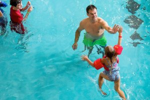 Leaping and reaching out, Braelyn Maus, 5, high fives her father Brad as they play in the pool during the Grand Opening of the Stanwood-Camano YMCA on Saturday, Sept. 3, 2016 in Stanwood, Wa. (Andy Bronson / The Herald)