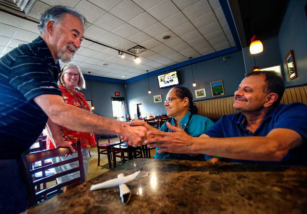 As Linda Witter and Ruqayya Bala enjoy the moment, Bill Witter (left) heartily shakes hands with Shabbir Bala while congratulating him on his retirement and the closure of Boondockers in Marysville Wednesday. (Dan Bates / The Herald)