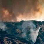 A helicopter makes a water drop amid black smoke rising from a wildfire burning in the Tujunga area of Los Angeles, seen from nearby Burbank, Calif., Friday afternoon, Sept. 1, 2017. Subdivisions full of houses are within a mile of the flames, and residents of three streets have been told to evacuate. (AP Photo/Richard Vogel)