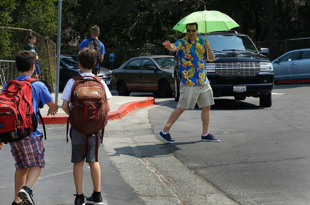 Josh Defeo wears an aloha shirt beneath the shade of an umbrella while directing the traffic of parents who came to pick up their children early at Orinda Intermediate School on Friday, Sept. 1, 2017, in Orinda, Calif. Dozens of cooling centers opened throughout California, schools let students out early and outdoor events were cancelled as temperatures soared from a heat wave expected to last through the Labor Day weekend. (AP Photo/Ben Margot)