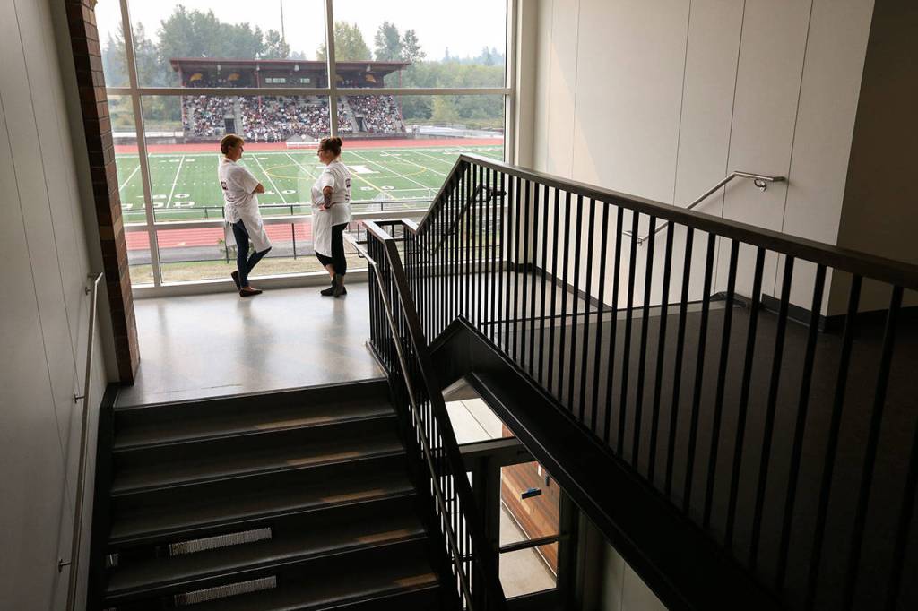 As students sit out on the football bleachers during orientation, kitchen staffers Laura Cannon (left) and Kari Albin chat in a stairway. (Andy Bronson / The Herald)