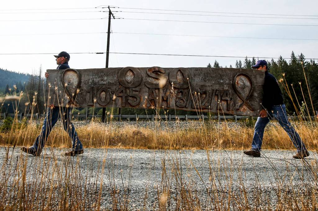 Oso firefighters Tim Harper (left) and Toby Hyde carry away a handmade Oso memorial sign before the removal of a Sitka spruce that it hung from on Saturday, Sept. 16. (Ian Terry / The Herald)