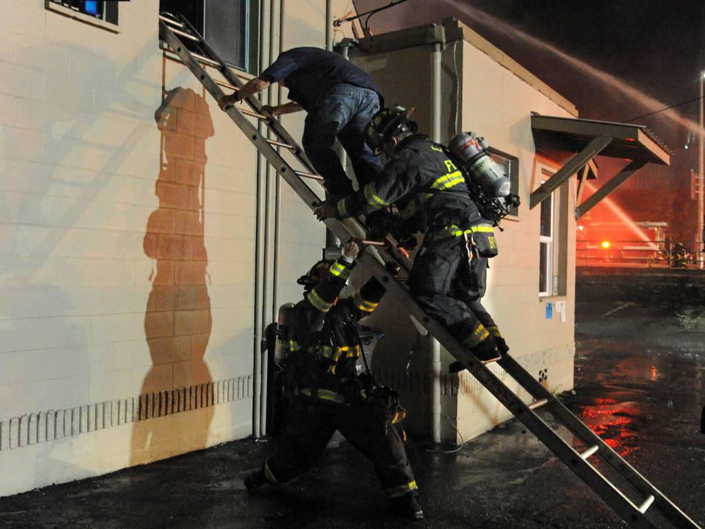 Firefighters help a man down a ladder during a three-alarm fire at Everett Office Furniture on Broadway on Monday. (Doug Ramsay / For The Herald)