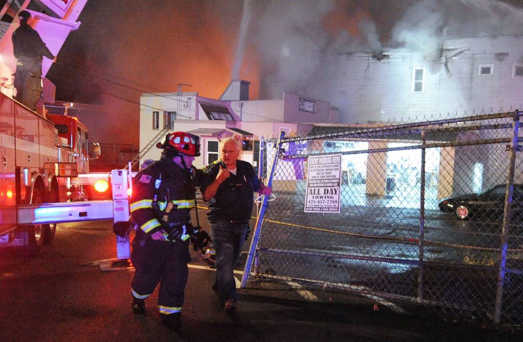 Firefighters escort a man away from the fire during at Everett Office Furniture on Monday. (Doug Ramsay / For The Herald)