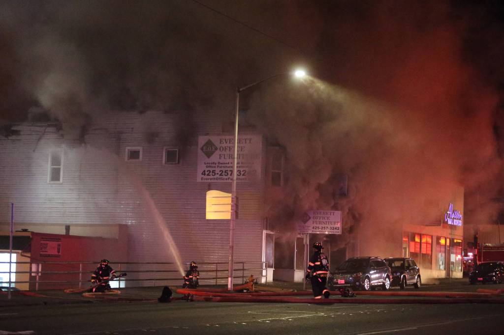 Firefighters pour water on the north side of the Everett Office Furniture building on Broadway as it burned Monday. (Andy Bronson / The Herald)