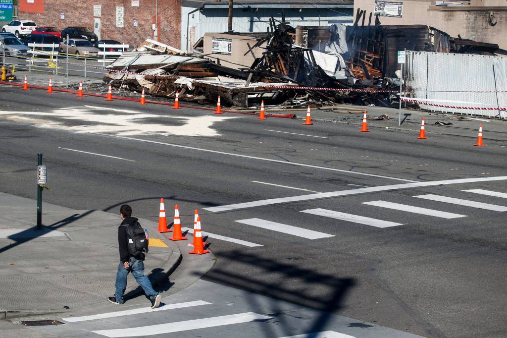 A pedestrian crosses Wall Street on Tuesday near Everett Office Furniture, which burned down on Broadway in Everett late Monday, Sept. 25. (Ian Terry / The Herald)