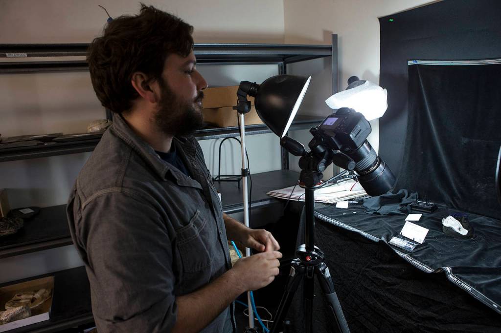 Sean Johnson photographs artifacts at FossilEra in Monroe. (Ian Terry / The Herald)
