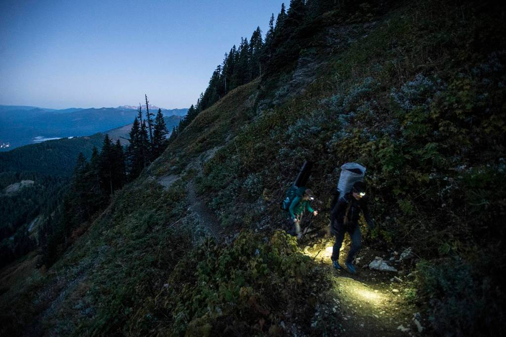 Under the faint blue glow of sunrise, Anastasia Allison and Rose Freeman journey, via headlamp, up Sauk Mountain. (Ian Terry / The Herald)