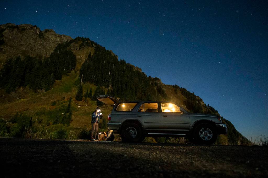 Anastasia Allison prepares her bag under a starry night before ascending Sauk Mountain, seen in the distance, with Rose Freeman to play music at sunrise on Oct. 5. (Ian Terry / The Herald)