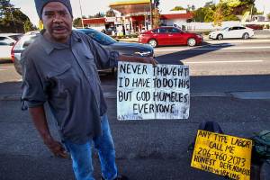 In Marysville, a 48-year-old man, who says people will know him as Houston, pulls his signs from his backpack and talks to The Herald about surviving homelessness. (Dan Bates / The Herald)