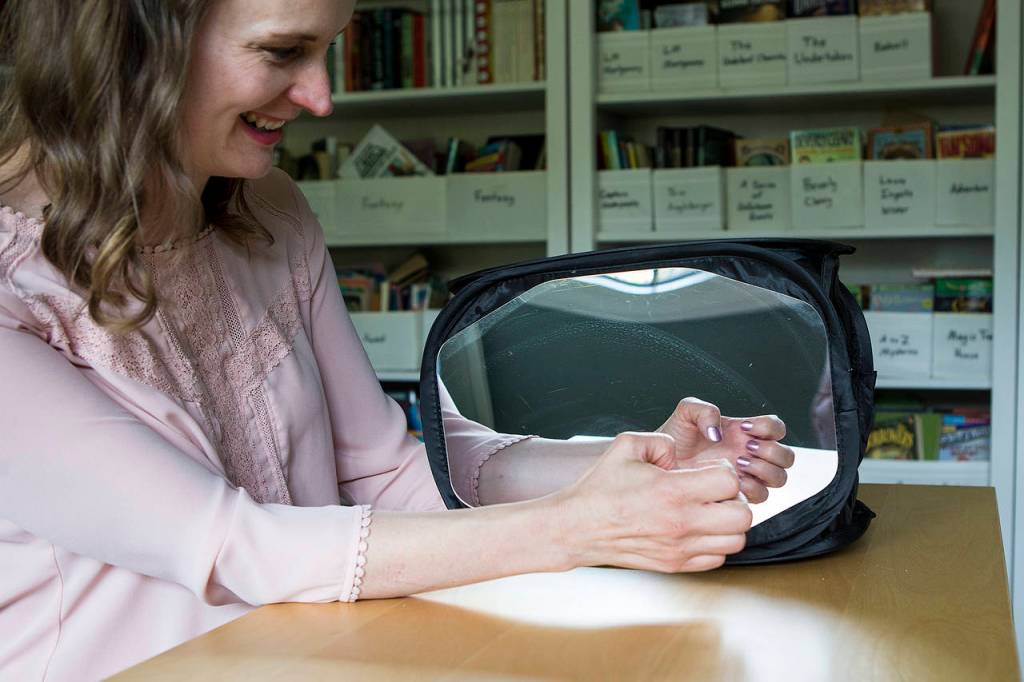 Jennifer Bardsley, of Edmonds, uses a mirror box to work through a range of motions with her hands. Bardsley broke her left wrist ice skating and has suffered from Complex Regional Pain Syndrome since the injury. (Ian Terry / The Herald)